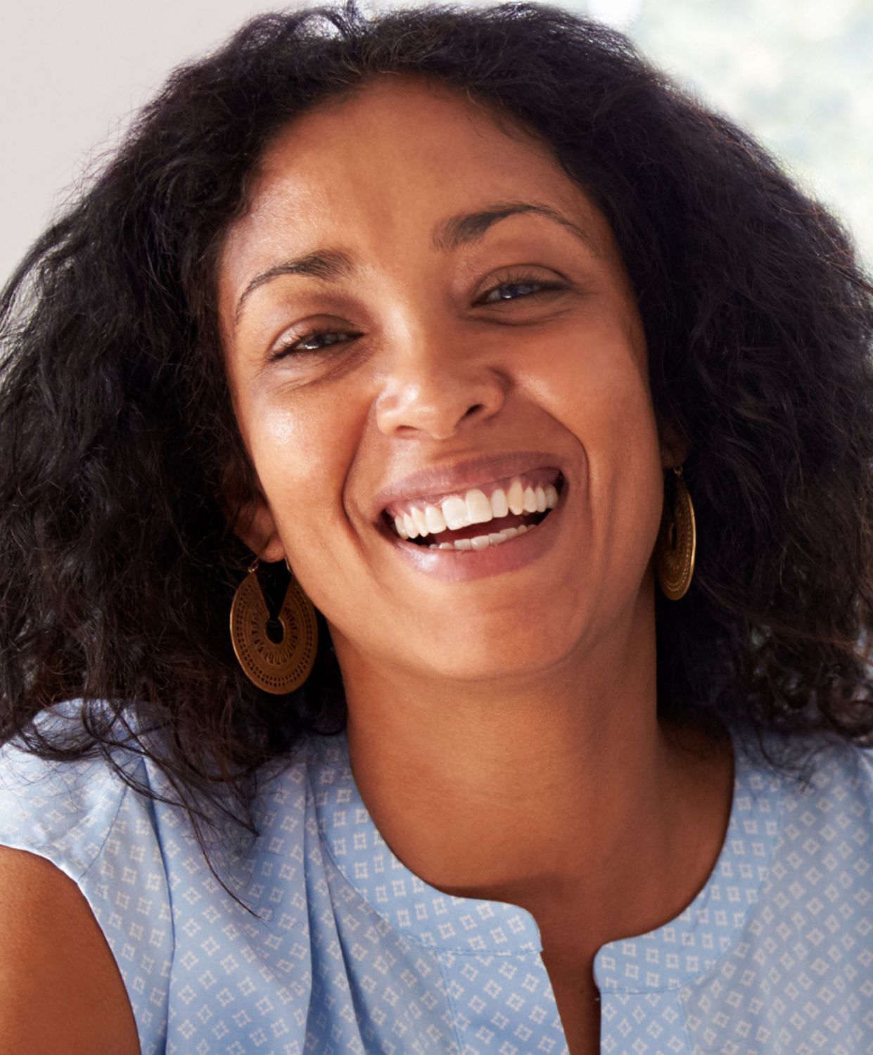 Smiling woman with curly hair and earrings.