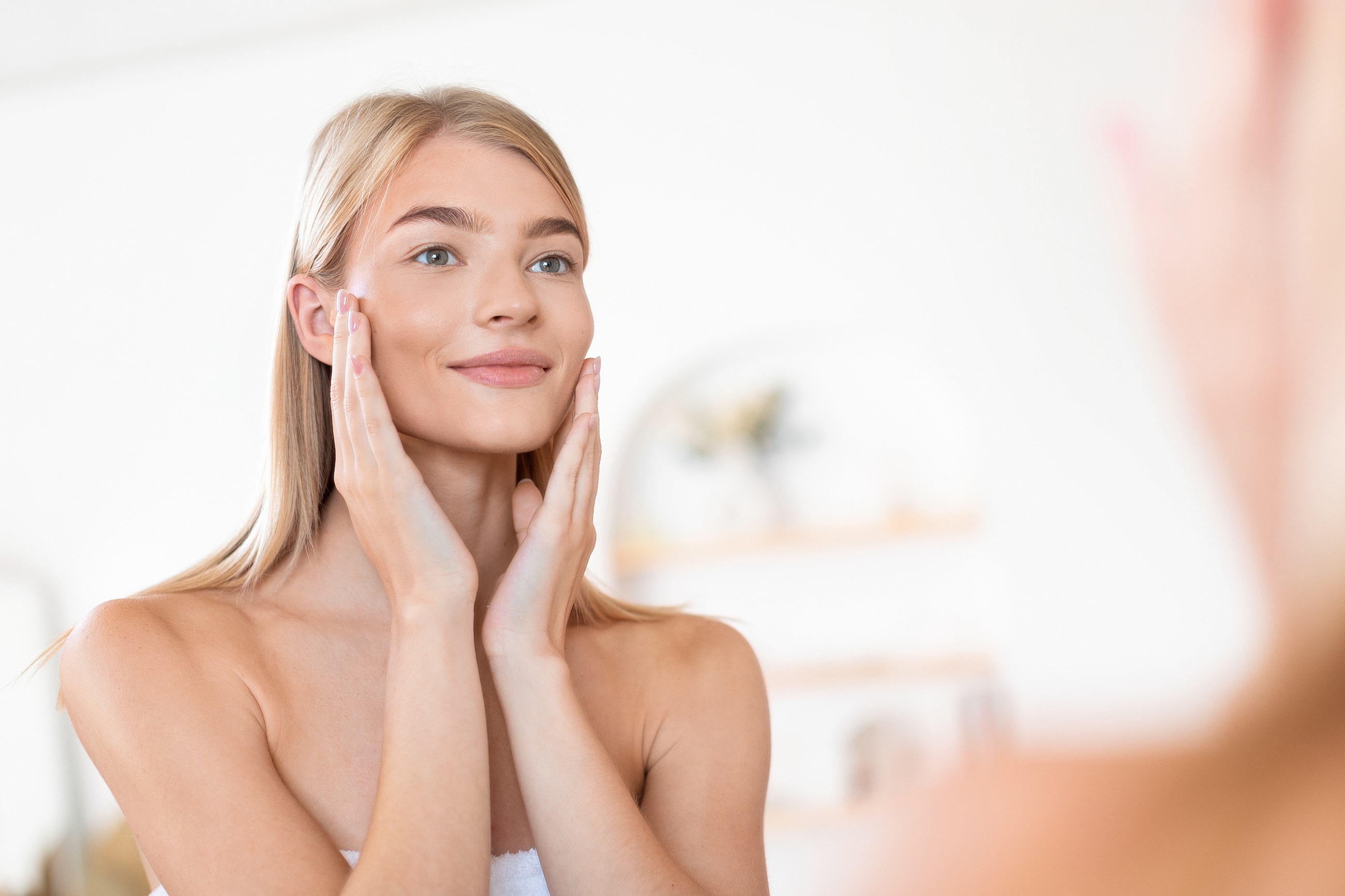 Young woman applying skincare in front of mirror.