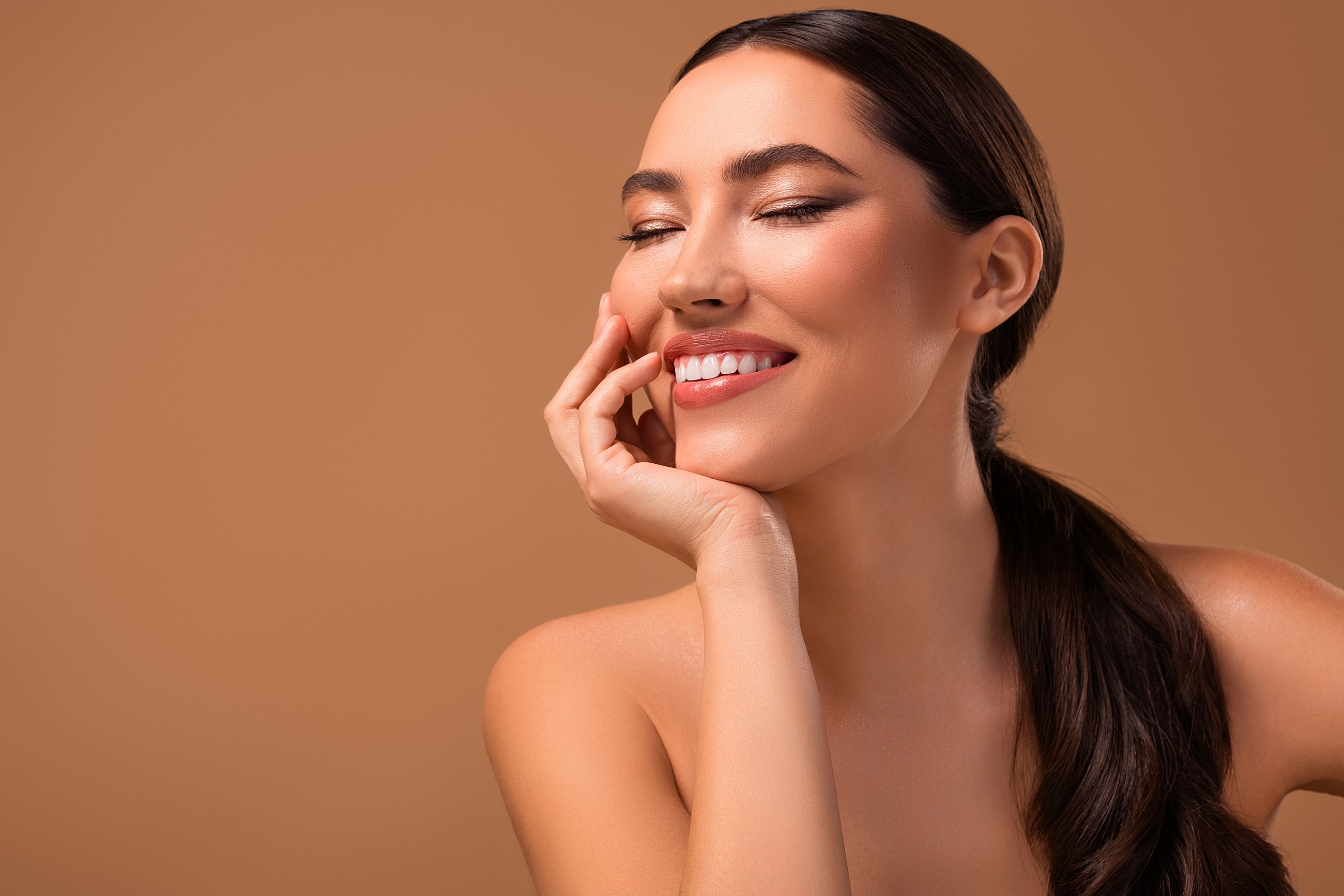 Smiling woman with glowing skin on brown background.